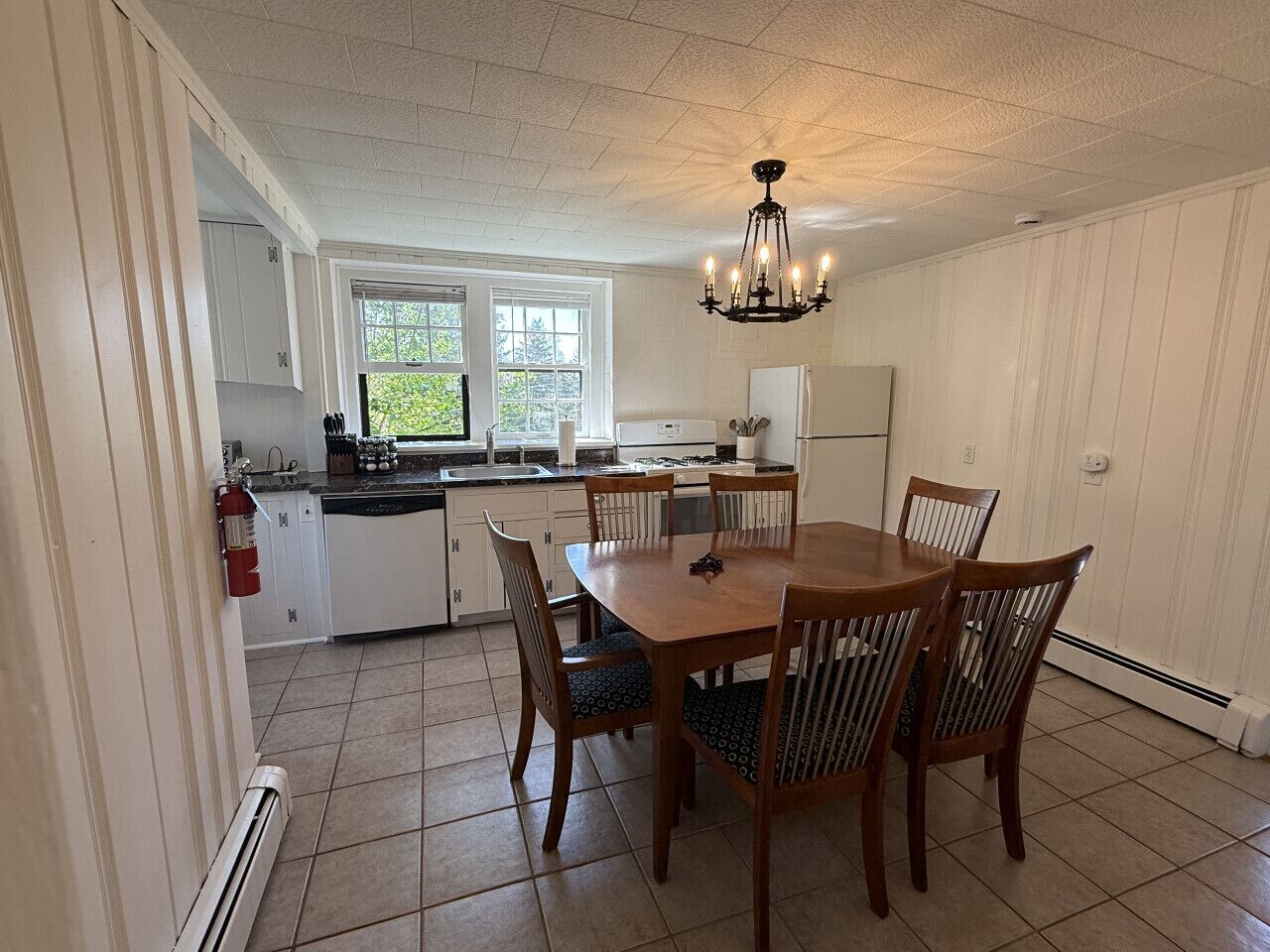 A kitchen with white cabinets, a dining table with chairs, a chandelier, and a fire extinguisher.