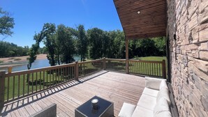 Una terraza techada con mobiliario exterior, una pared de piedra y vistas a un río y árboles.