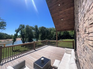 Eine überdachte Terrasse mit Gartenmöbeln, einer Steinmauer und Blick auf einen Fluss und Bäume.
