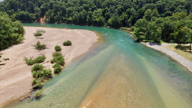 Un río de aguas claras, rodeado de un bosque verde frondoso y una zona de playa arenosa.