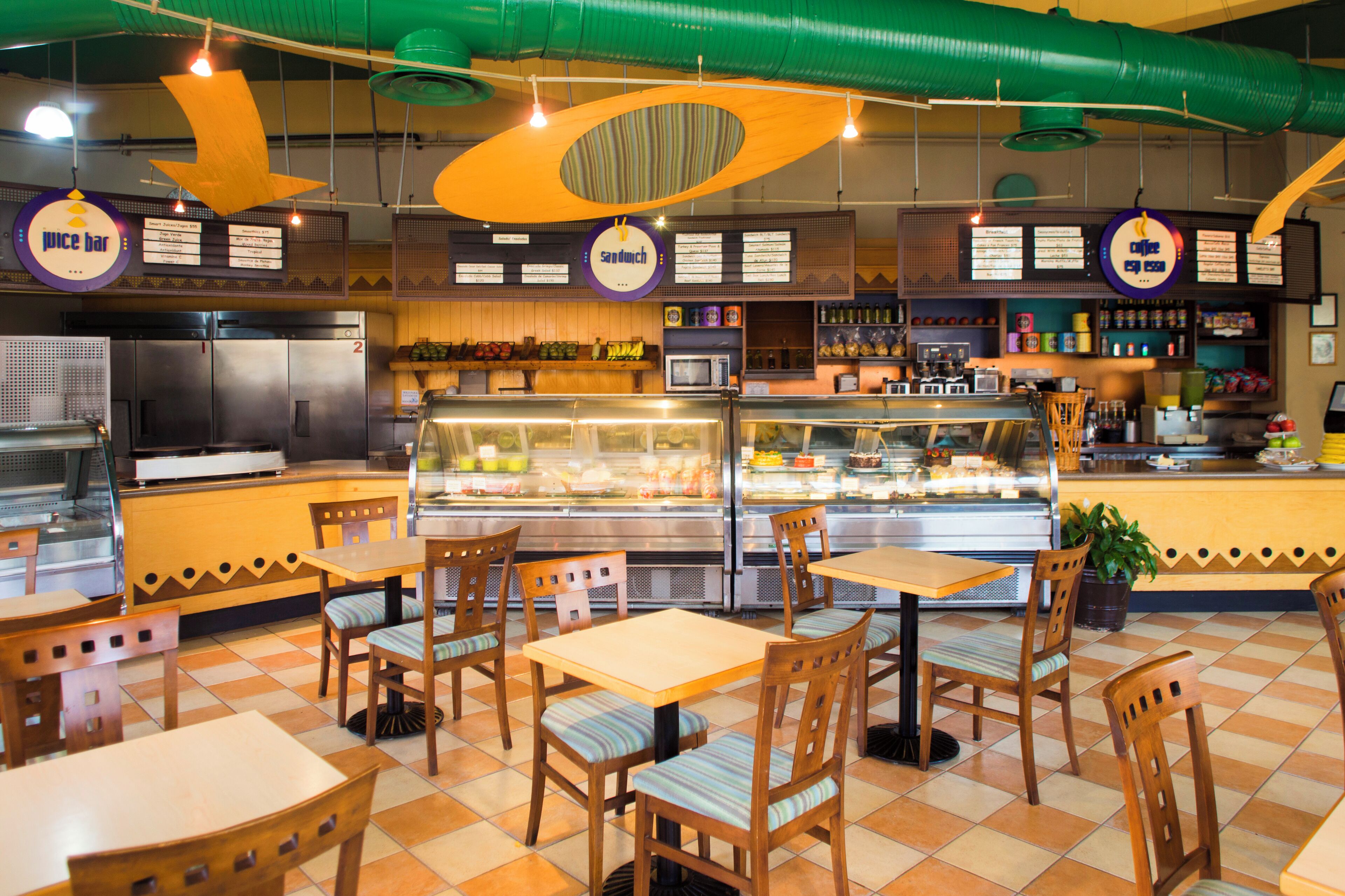A restaurant with a checkered floor, wooden tables and chairs, a counter with a display case, and hanging signs.