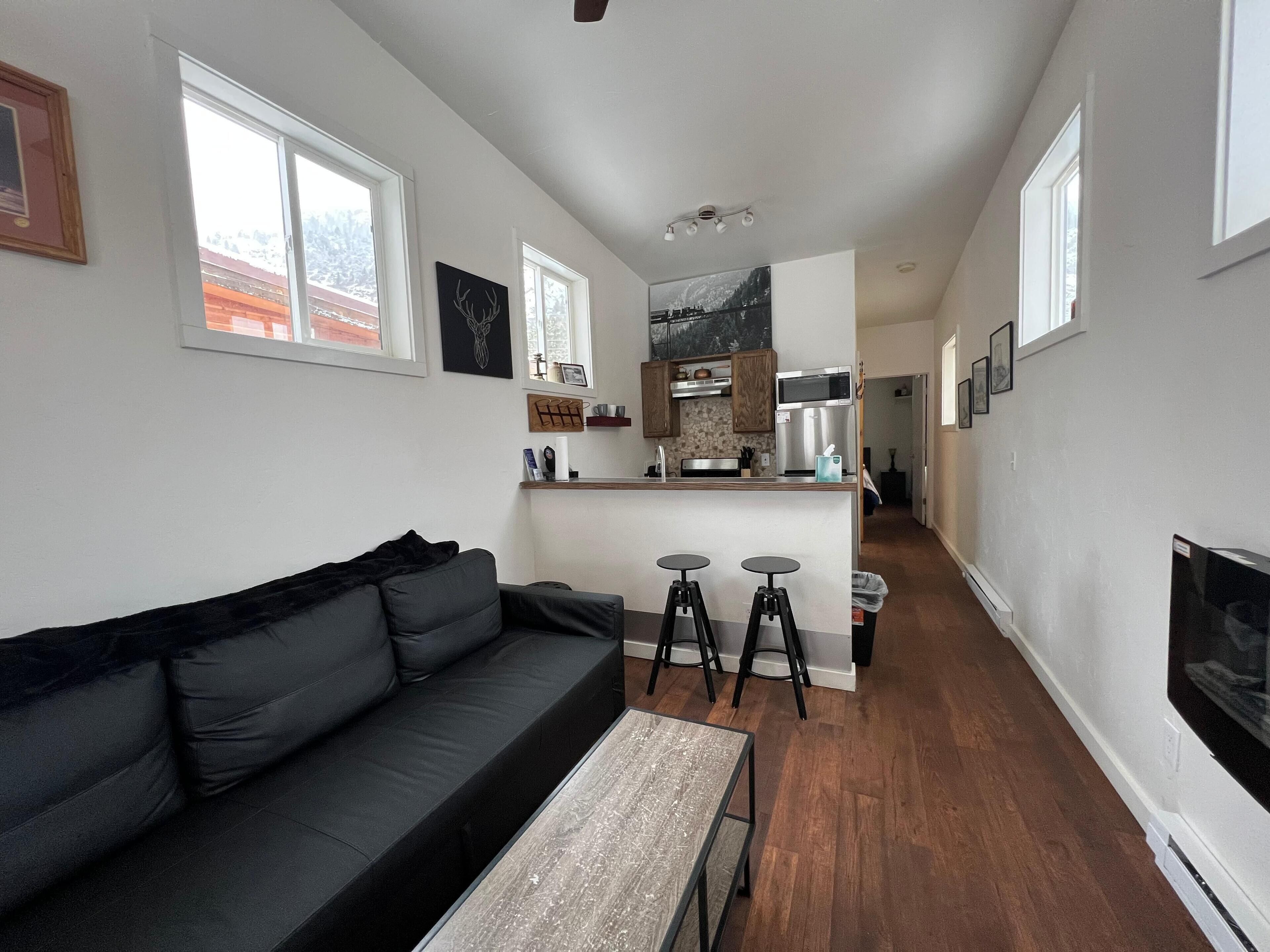 A modern living room with a black sofa, a coffee table, and a kitchen area with a microwave and a stove.