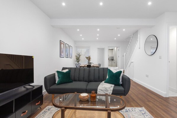 A modern living room with a sectional sofa, a flat-screen TV, a glass coffee table, and a staircase leading to an upper level.