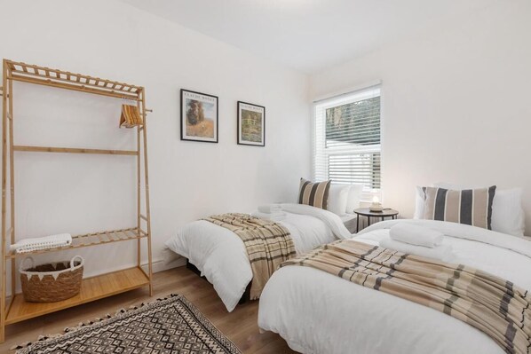 Un dormitorio con dos camas, una estantería de madera y una ventana con persianas.