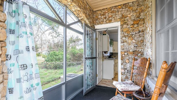 Ein gemütliches Zimmer mit Steinwand, einem Fenster mit Blick auf Grünflächen, einem Holzstuhl und einem gemusterten Vorhang.