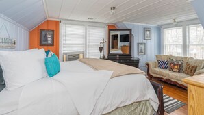 Ein Schlafzimmer mit Bett, einer Couch, einem Spiegel und einem Fenster mit Jalousien.