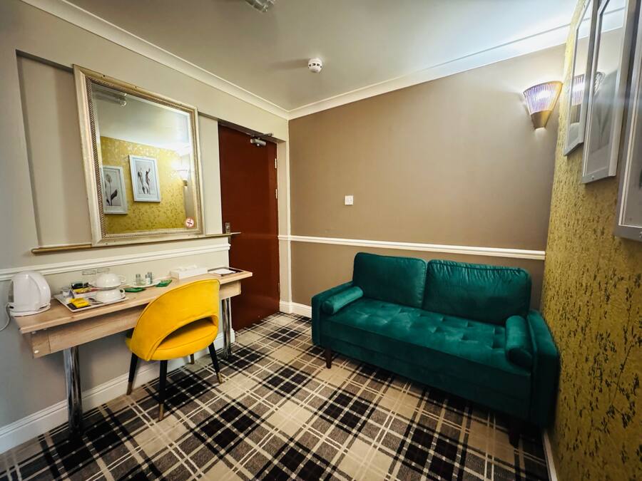 A room with a plaid carpet, a yellow chair, a green sofa, a desk with a mirror, and a door.