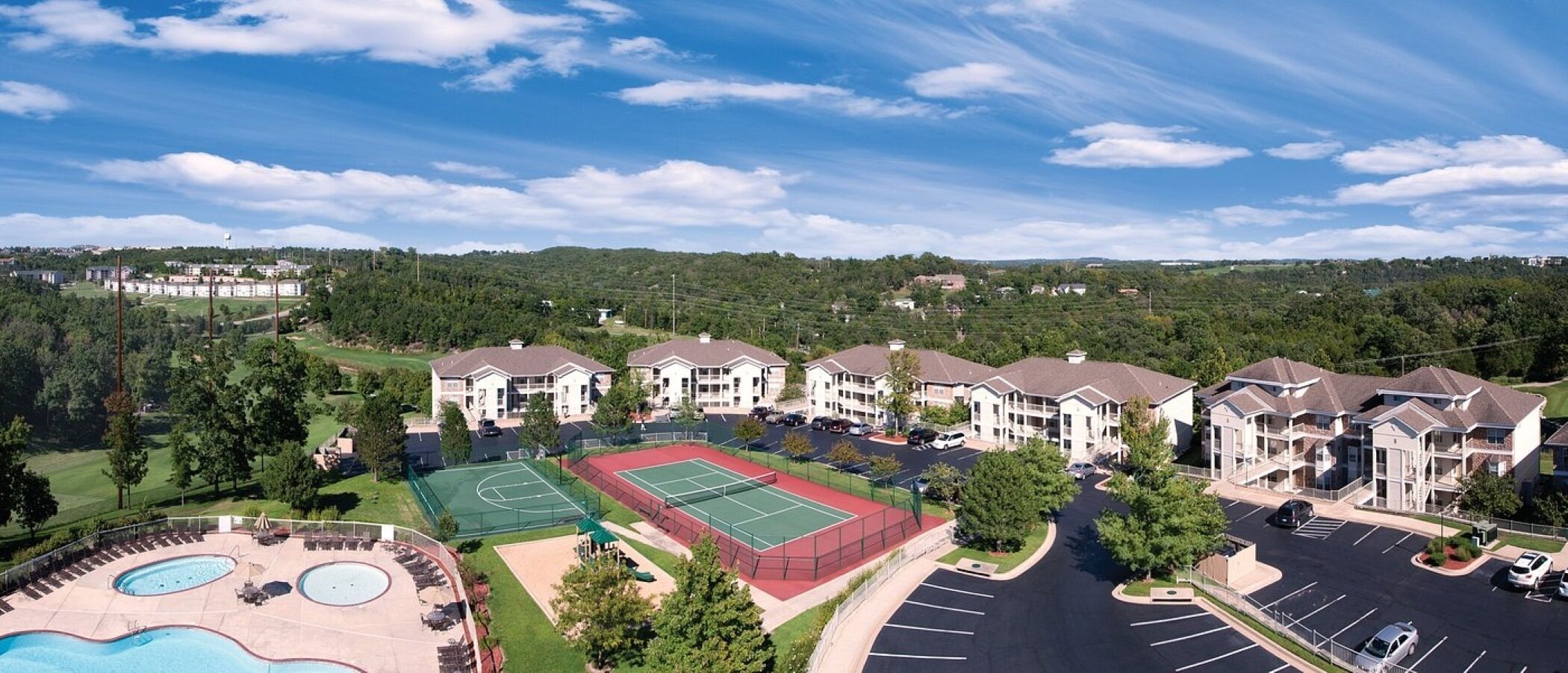 A residential complex with multiple apartment buildings, a tennis court, and a swimming pool.