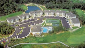 Vue aérienne d’un terrain de golf avec un ensemble de bâtiments résidentiels, comprenant un espace de stationnement et une piscine.