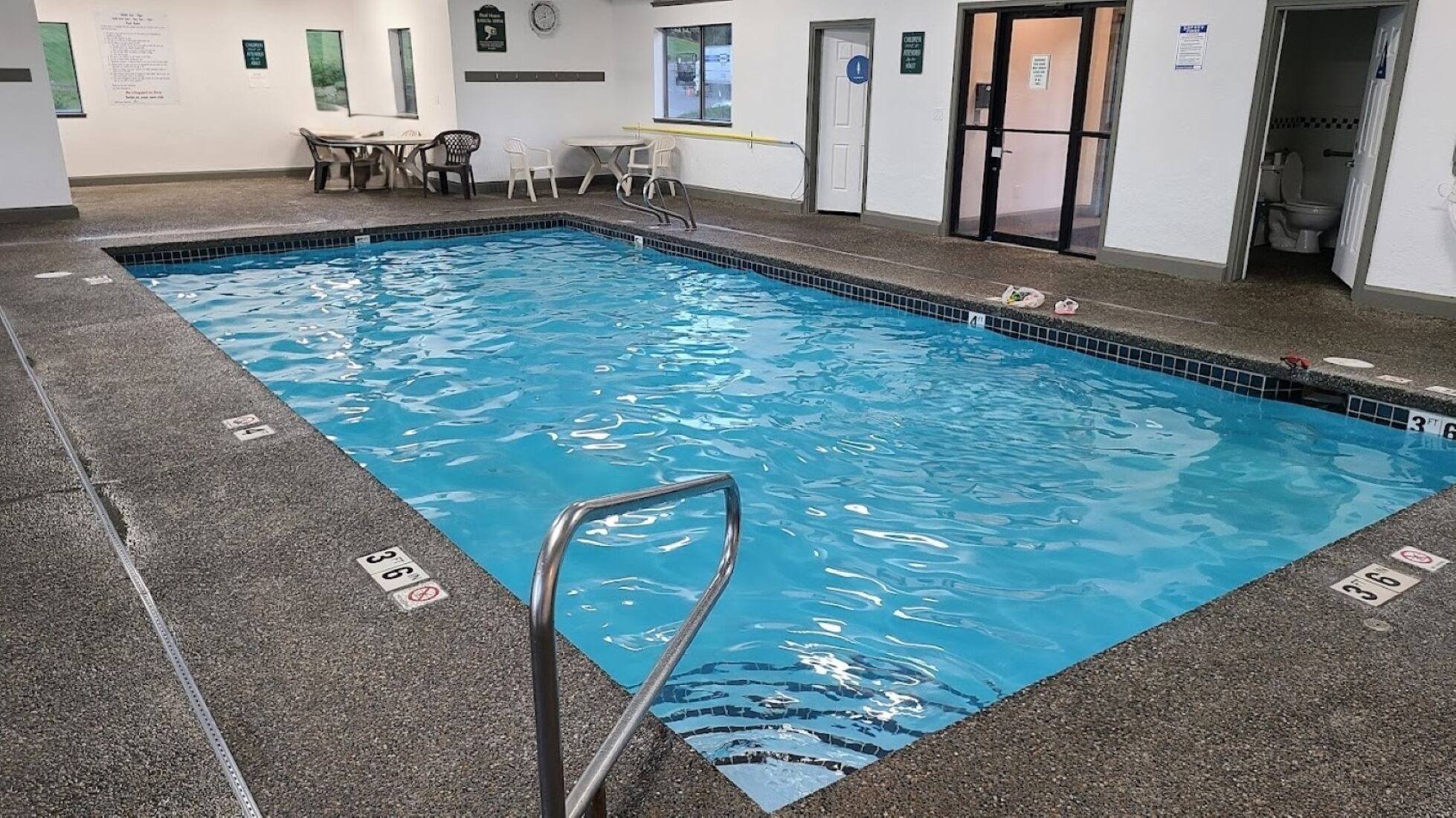 An indoor swimming pool with a clear water surface, marked depth lines, and a pool ladder.