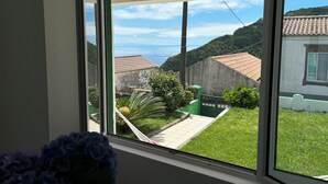 Blick durch ein Fenster auf ein Gebäude mit einem Ziegeldach, einen grünen Rasen und eine ferne Meerlandschaft.