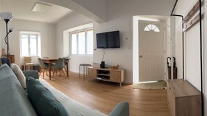Un salon moderne avec un canapé, un coin repas avec des chaises, un téléviseur fixé au mur et un meuble en bois.