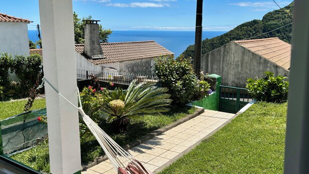 Blick vom Balkon auf einen Garten mit Hängematte, Pflasterterrasse und Meerblick.