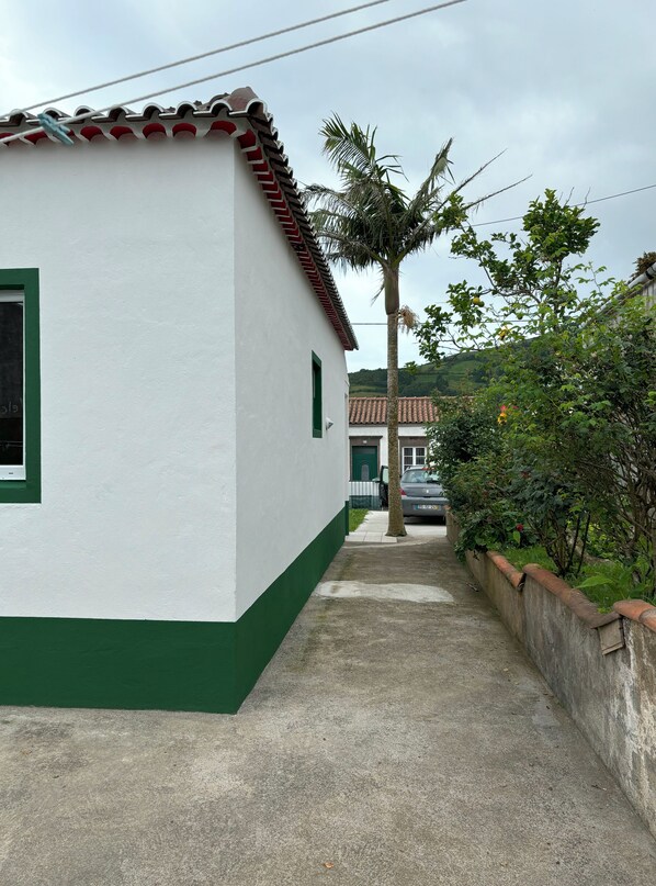 Un étroit chemin de béton mène à un bâtiment blanc, doté d’un soubassement vert et d’un toit recouvert de tuiles.