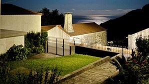 Ein Nachtblick auf ein Wohngebiet mit einem Haus, einem gepflasterten Weg und Blick auf das Meer unter dem Vollmond.