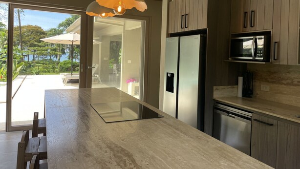 A modern kitchen with wooden cabinets, a stainless steel refrigerator, a built-in microwave, and pendant lighting.