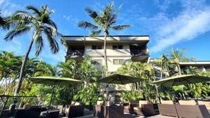 Un hôtel à la structure de deux étages, doté d’un espace extérieur aménagé avec des parasols et des palmiers.