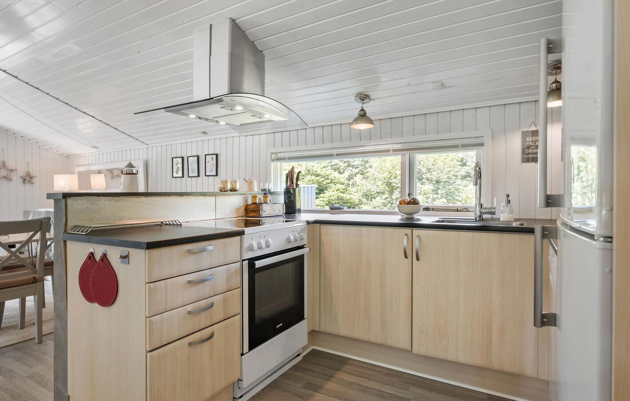 Een moderne keuken met houten kastjes, een roestvrijstalen afzuigkap en een raam dat voor natuurlijk licht zorgt.