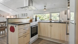 A modern kitchen with wooden cabinets, a stainless steel range hood, and a window providing natural light. - 3 bedroom nice home in Fjerritslev (Fjerritslev)