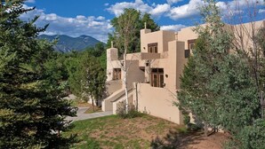 Un edificio moderno con techo plano, múltiples ventanas y un paisaje circundante con árboles y montañas.