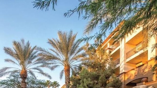 Una piscina con caída de agua, rodeada de palmeras y un edificio con balcones.