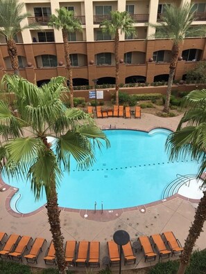 A swimming pool surrounded by palm trees and orange lounge chairs, with a multi-story building in the background. - Las Vegas | VIP Vegas Retreat | Pool + Hot Tub | 3BR Sleeps 6 (Las Vegas)