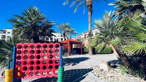 Estructura de parque infantil roja y azul con varios agujeros, rodeada de palmeras y un cielo azul despejado.