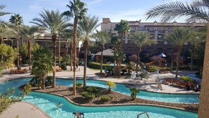 Zona de piscina en un resort con varias piscinas, palmeras y sillones de descanso.