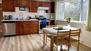 Una cocina con armarios de madera, lavavajillas, horno y una mesa de comedor con sillas.