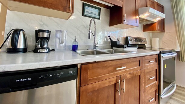 Una cocina moderna con armarios de madera, lavavajillas de acero inoxidable, cafetera y un lavabo.
