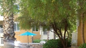 Un chemin pavé, un palmier, un parasol bleu et un bâtiment à la façade en briques.