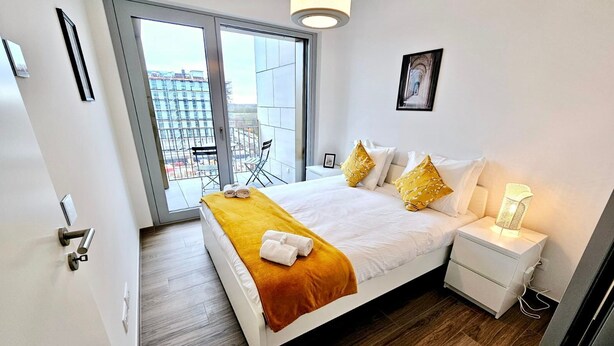 Ein modernes Hotelzimmer mit einem großen Bett, einem Nachttisch, einem Fenster mit Blick auf Gebäude und einer Tür mit Griff.
