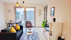 Ein modernes Wohnzimmer mit einer schwarzen Couch, einem Esstisch, einem gemusterten Teppich und Blick auf die Stadt durch große Fenster.