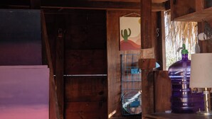 A rustic wooden interior with a high ceiling, a bed with a hanging decoration, a small bar area, and a window with a view. - Beachfront Tiny Home on the La Fortuna Surf Break - The Baja Station (San José del Cabo)