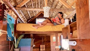 A compact, rustic room with a wooden ceiling, a bunk bed, a small desk, a chair, a potted plant, and a stove. - Beachfront Tiny Home on the La Fortuna Surf Break - The Baja Station (San José del Cabo)