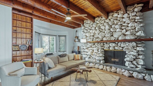 Un salón acogedor con chimenea de piedra, vigas de madera en el techo, una estantería y un sofá cómodo.
