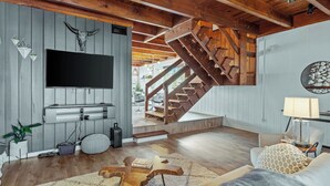 Una sala de estar moderna con una escalera de madera, un televisor montado y una zona de estar acogedora.