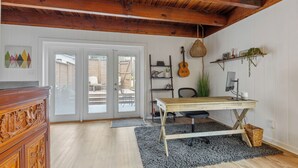 Una habitación con techo de madera, un escritorio con una computadora, una guitarra y una planta.