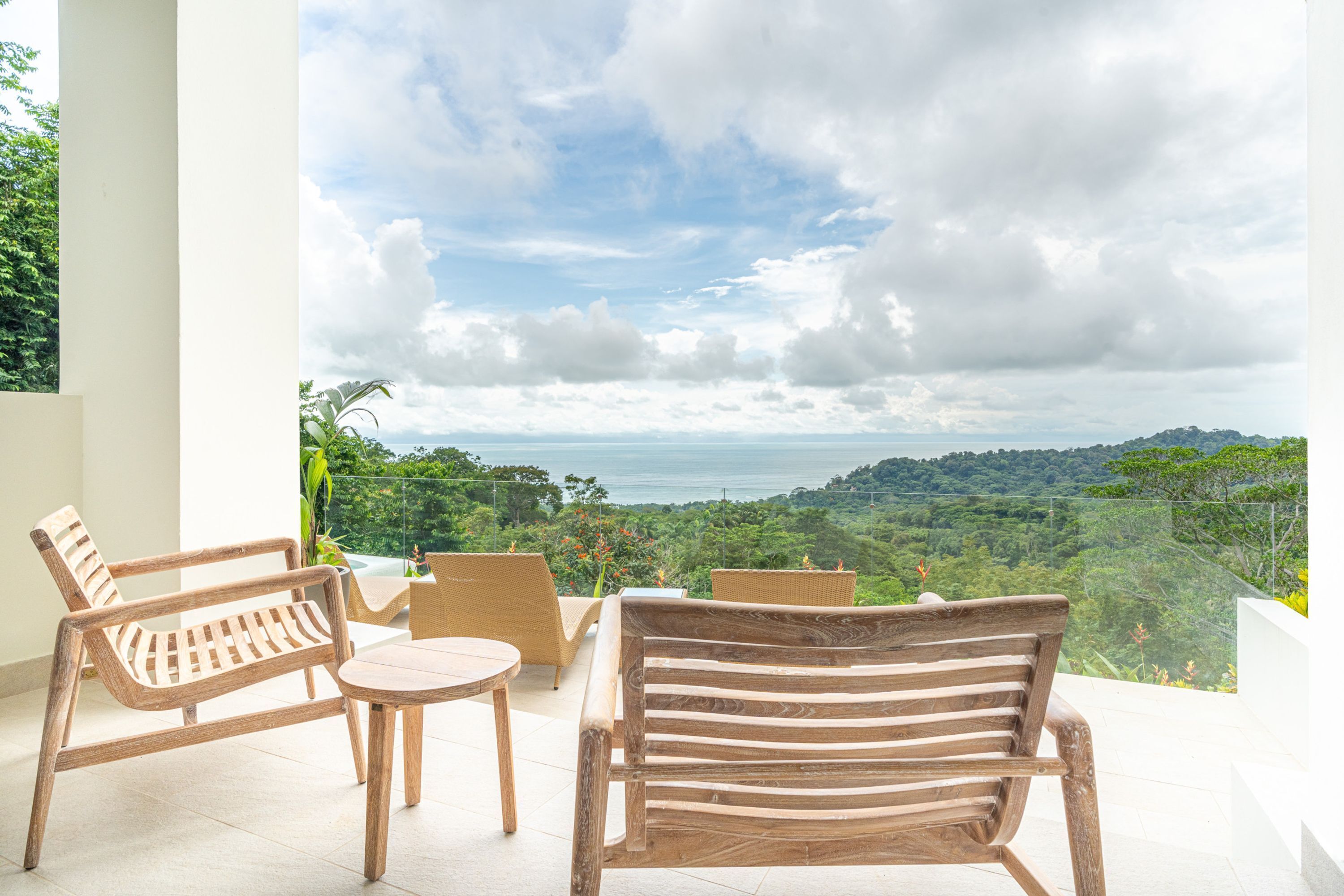 A balcony with wooden furniture and a view of a lush landscape and the sea.