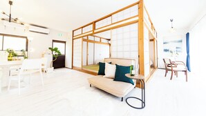 A modern hotel room with a wooden bed frame, a sofa, a dining area with a table and chairs, and a view of the outdoors. - Awaji Large Log House in Goshiki 2 (Sumoto)