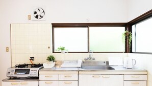 A kitchen with a gas stove, a microwave, a sink, and a window with plants. - Awaji Large Log House in Goshiki 2 (Sumoto)