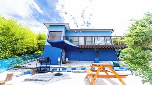 A modern blue building with a patio, a barbecue grill, and a wooden table. - Awaji Large Log House in Goshiki 2 (Sumoto)