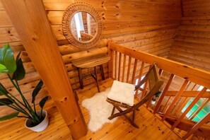 A cozy cabin interior with a wooden bench, a chair with a cushion, a mirror on the wall, and a potted plant. - Awaji Large Log House in Goshiki 2 (Sumoto)