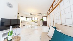A modern living room with a flat-screen TV, a sofa, and a dining area in the background. - Awaji Large Log House in Goshiki 2 (Sumoto)