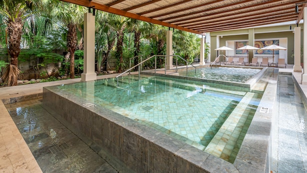 Ein Poolbereich mit zwei Pools, Palmen und Liegestühlen unter einer Holzpergola.