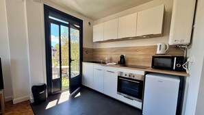 A modern kitchen with a built-in microwave, oven, and coffee maker, a sliding glass door to a balcony, and a compact refrigerator. - Casa #1407 - T2 - Climatisé avec Balcon - Centre-ville (Brive-la-Gaillarde)