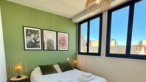 A bedroom with a bed, green walls, framed artwork, a window with a view, and a hanging light fixture. - Casa #1407 - T2 - Climatisé avec Balcon - Centre-ville (Brive-la-Gaillarde)