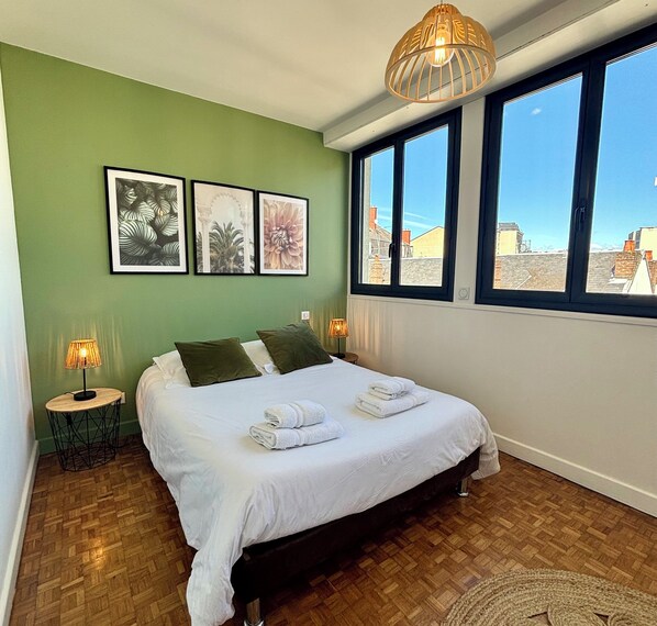 Una camera da letto con un letto, pareti verdi, opere d'arte incorniciate, una finestra con vista e una lampada a sospensione.