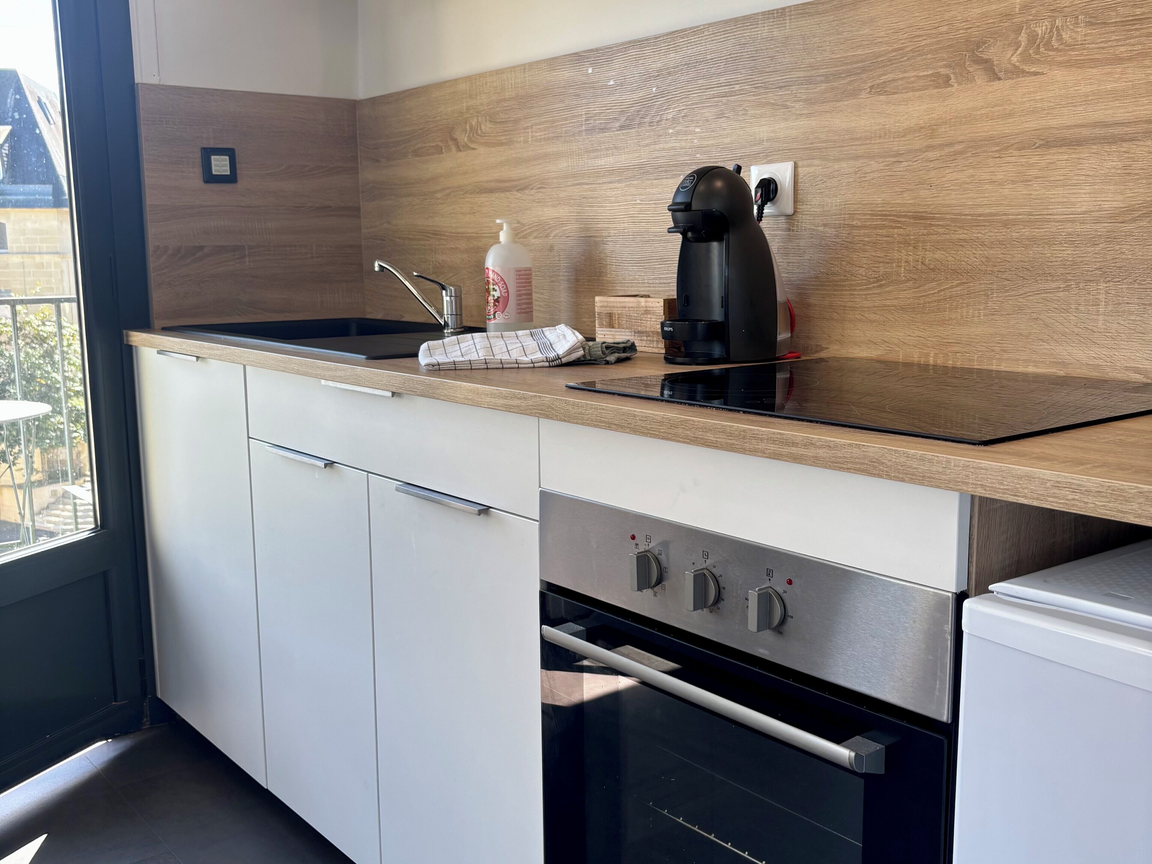 Cozinha moderna com bancada de madeira, máquina de café, chaleira e forno embutido.