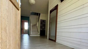 Un couloir avec une porte en bois, un paillasson, un escalier et une bibliothèque.